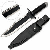 Rambo First Blood Part II knife prop replica full hero view on mossy log showing black matte coated blade with serrated saw-tooth spine polished silver bevel RAMBO FIRST BLOOD PART II engraving black crossguard black cord-wrapped handle and knurled silver pommel cap – movie display collectible