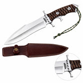 Rambo V Last Blood Heartstopper knife prop replica held in gloved hand on mossy rock in sunlit green jungle forest showing silver satin display finish double-edged dagger blade with RAMBO LAST BLOOD engraving dark walnut crosshatch handle and silver steel double crossguard – John Rambo 2019 movie display collectible