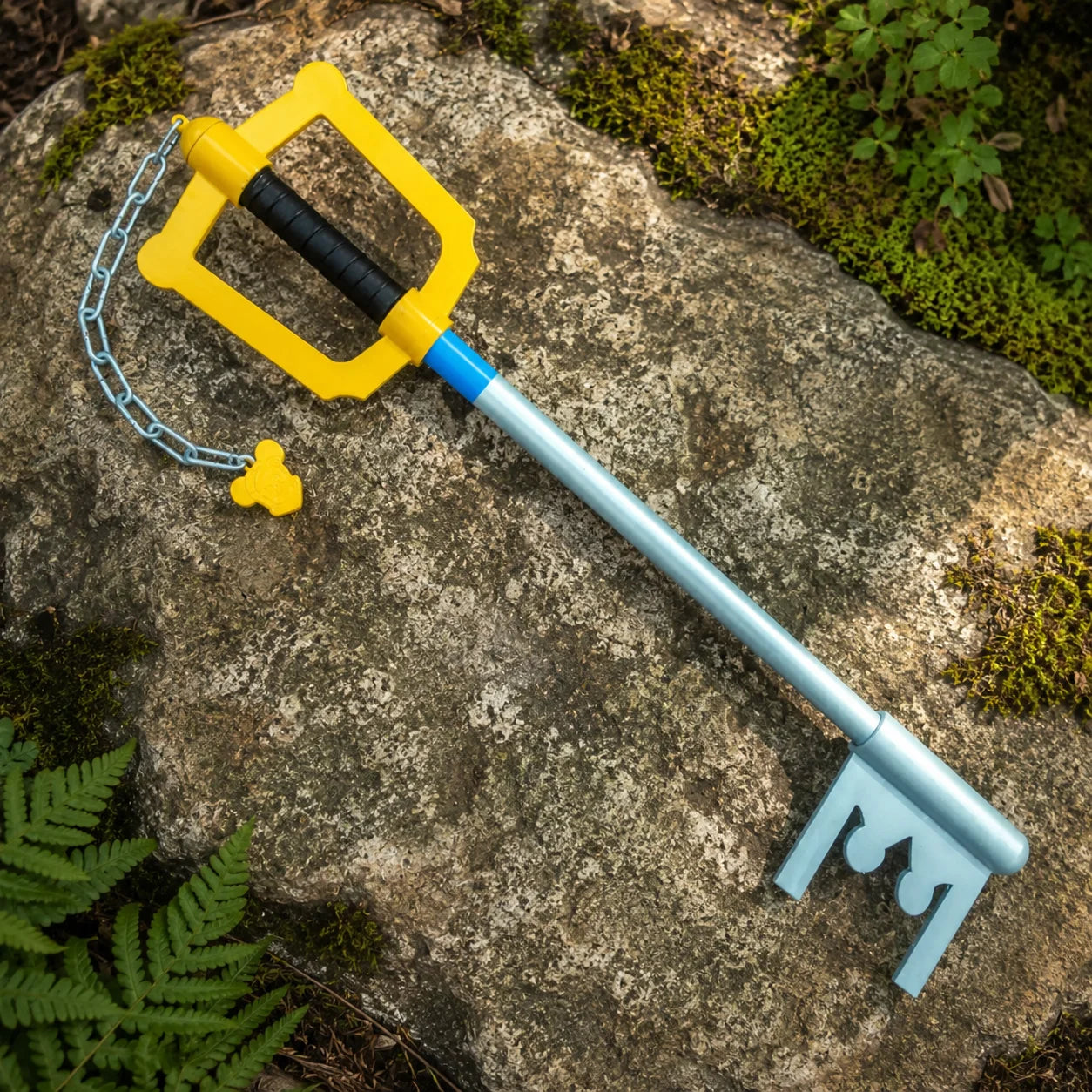 Kingdom Hearts Sora Keyblade prop replica lying on mossy forest ground – game collectible display piece