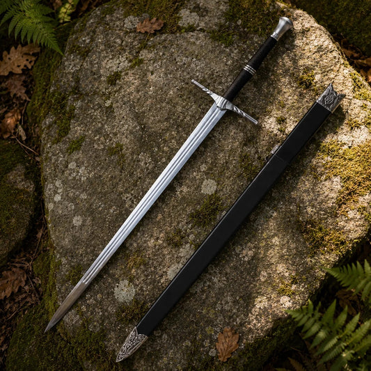 Geralt of Rivia steel sword prop replica full length diagonal propped on mossy log in sunlit fern forest showing complete polished silver blade with triple fuller grooves ornate silver crossguard twisted quillons and black cord-wrapped grip – The Witcher fan gift