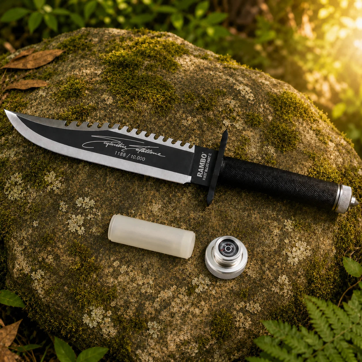 Rambo First Blood Part II Stallone Signature Edition knife prop replica alternate hero angle on mossy rock showing complete black matte blade with serrated spine polished silver bevel black crossguard black diamond crosshatch knurled handle and knurled silver pommel cap in sunlit green jungle forest – Rambo movie collectible cosplay prop