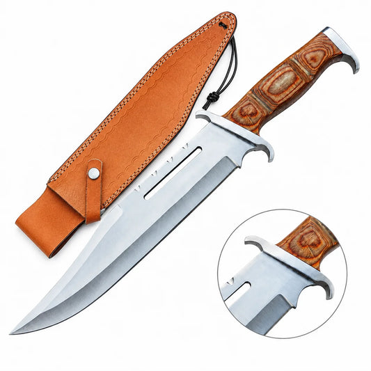 Rambo III Bowie knife prop replica held in gloved hand in sunlit green jungle forest showing silver satin display finish clip-point bowie blade with 2 elongated rectangular blade slots near ricasso and warm honey brown pakkawood handle with silver bolster panels – John Rambo 1988 movie display collectible